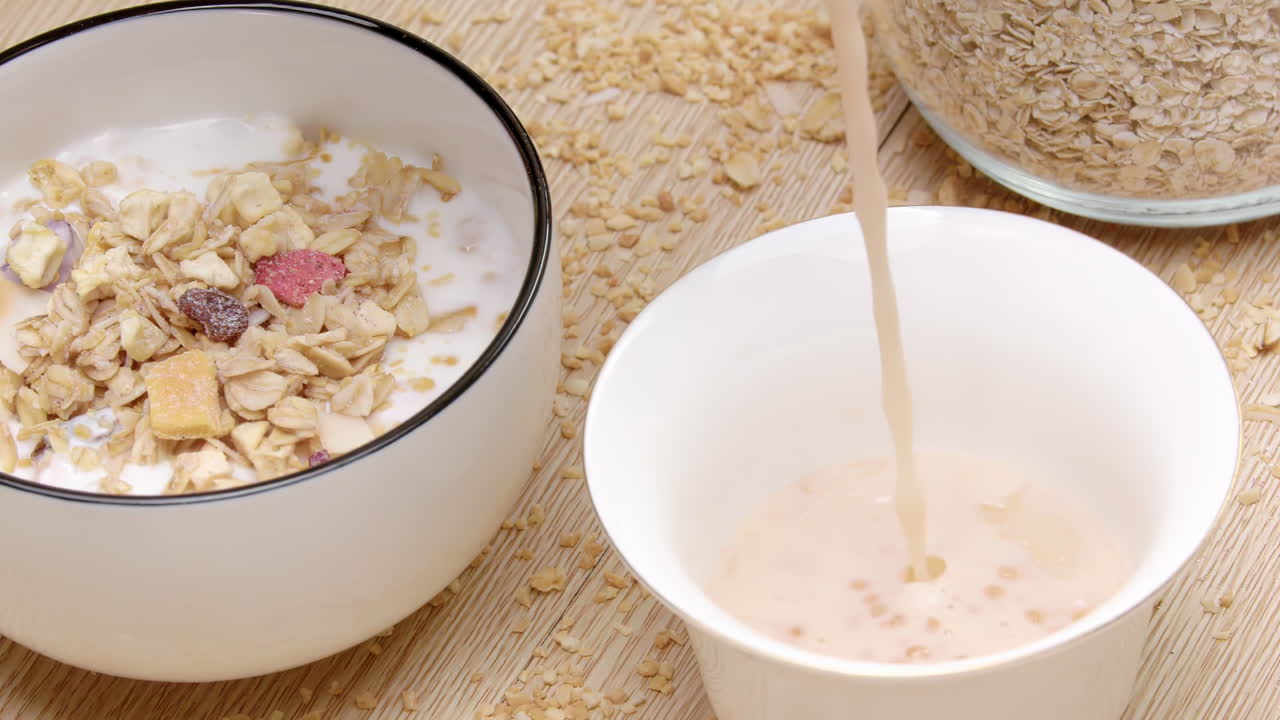 Un filo di latte o yogurt cremoso si versa in una ciotola accanto a croccanti cereali colorati guarniti, questa colazione nutriente e salutare, pubblicità di prodotti lattiero-caseari.