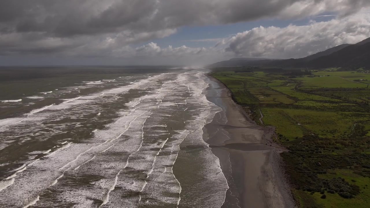 Prise de vue aérienne par drone en reculant au-dessus d'une plage de la mer de Tasman en Nouvelle-Zélande, avec de longues vagues.