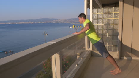 Mann-Beginnt-Liegestütze-Auf-Dem-Balkon-Mit-Meerblick-Im-Hintergrund