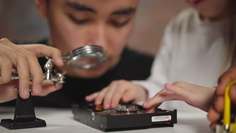 asian teacher adjusts magnifying glass and girl turns disk