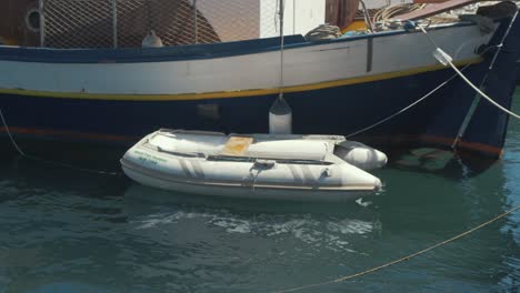 small plastic dinghy tied to larger carvel built wooden sail boat in harbor