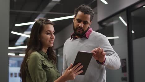 Diverse-female-and-male-work-colleagues-standing-looking-at-tablet-together-and-talking