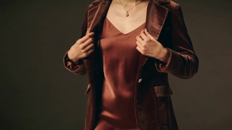 Sistemare la modella su segnale, aprire il blazer, rivelare il vestito color bronzo, lisciare il tessuto, presentare l'abito
