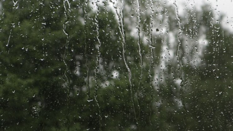 Gotas de lluvia cayendo sobre la superficie de una ventana y deslizándose hacia abajo durante un día nublado, primer plano estático.