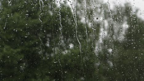 rain drops falling on window surface and slidding down during overcast day, close-up still shot