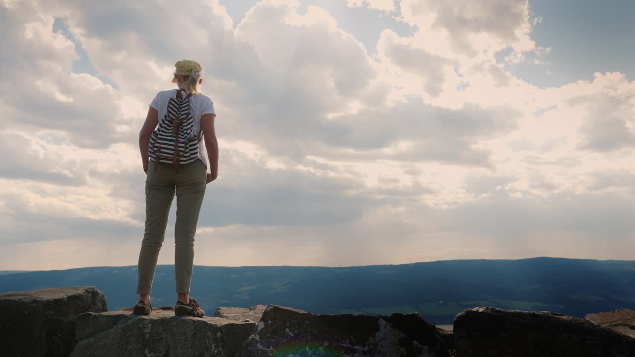 여성 여행자는 아래 서사시적인 하늘을 배경으로 서 있습니다.