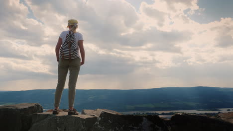 The-Female-Traveler-Stands-Against-The-Background-Of-The-Epic-Sky-Below-Is-The-River-And-The-Town-Of