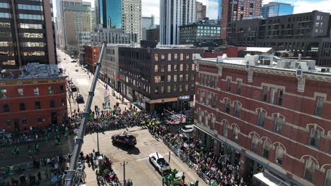 Drone-shot-tilting-down-from-the-Denver-city-skyline-to-reveal-parade-floats-driving-through-downtown-Denver-for-Saint-Patrick's-Day