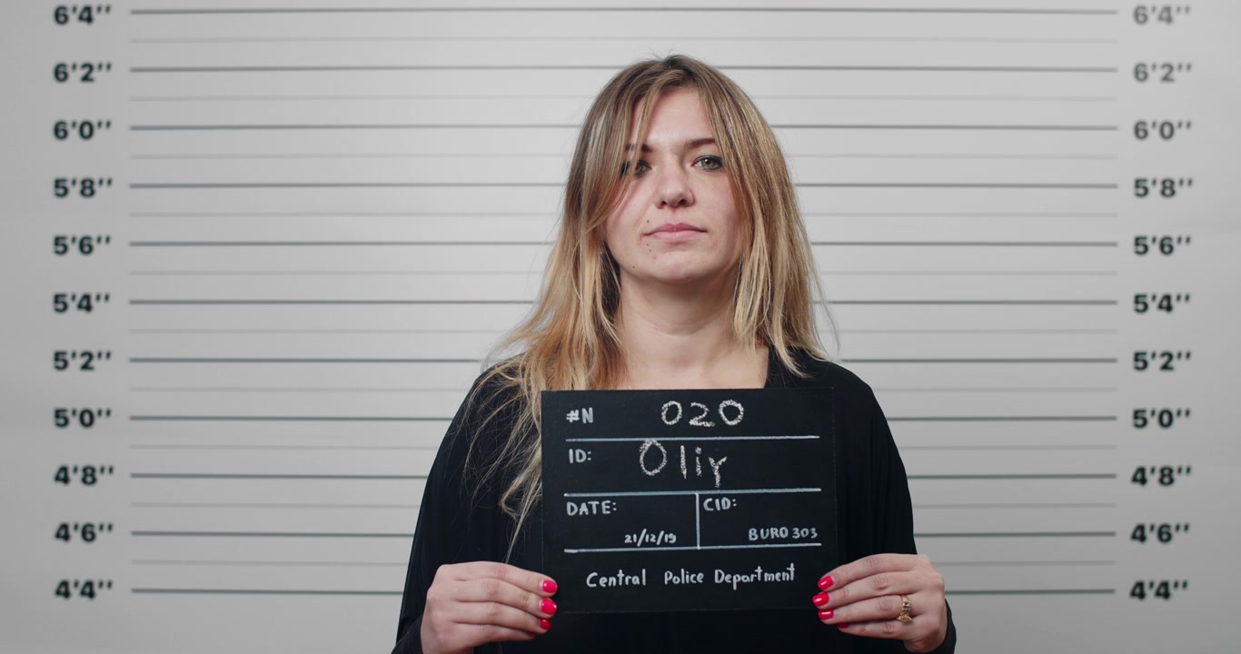 Young Woman Holding Mugshot Board in Police Station