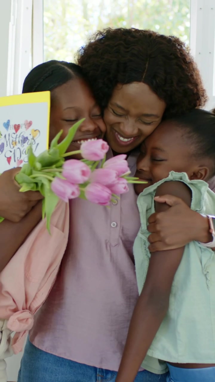 Vídeo vertical: Filhas surpreendendo a mãe com cartão e tulipas na cozinha, mãe abraçando