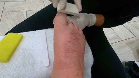 professional pedicurist buffs and smooths the toes on a man's right foot using a buffer board