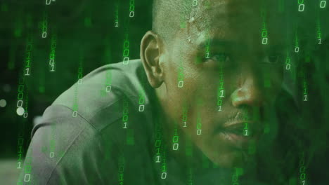 Binary code overlaying man's face, concentrating on digital work in office setting