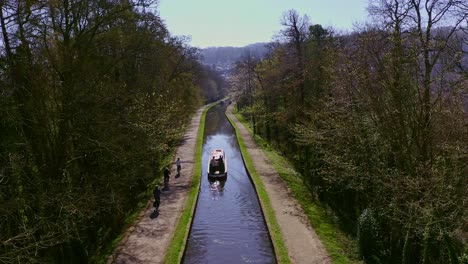 Un-Barco-Estrecho-Que-Se-Dirige-Río-Arriba-Después-De-Cruzar-El-Acueducto-Pontcysyllte,-Diseñado-Por-Thomas-Telford,-Ubicado-En-La-Hermosa-Campiña-Galesa,-Famosa-Ruta-Del-Canal-Llangollen,-Mientras-Los-Ciclistas-Pasan