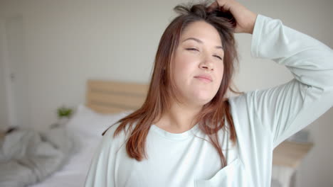 Thoughtful-plus-size-biracial-woman-looking-out-of-bedroom-window-in-the-morning,-slow-motion