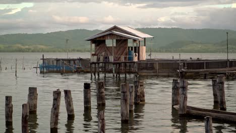 a tiny stilted hut in the water's edge overlooking picturesque mountains