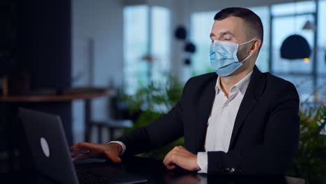 man in suit putting on mask while sitting at the table. businessman opens and clothes laptop, tries to open it again and fails. close up.