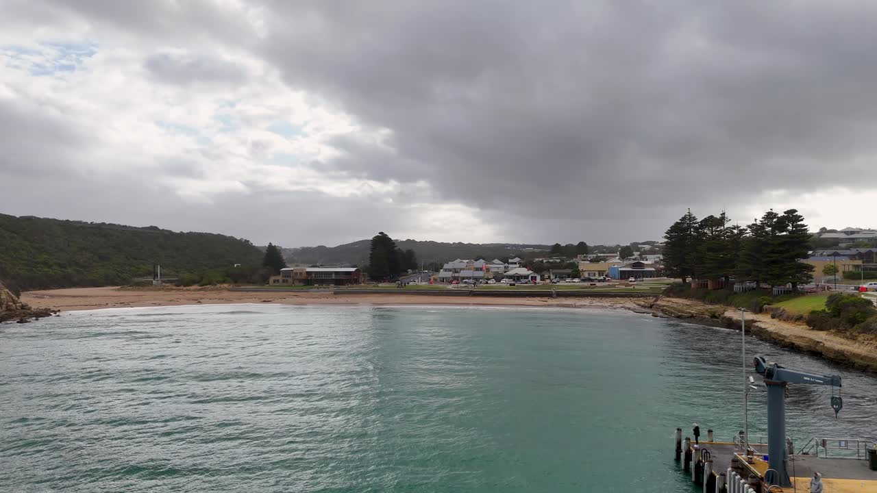 Drone footage captures Port Campbell's scenic coastline, showcasing the town, beach, and ocean under cloudy skies