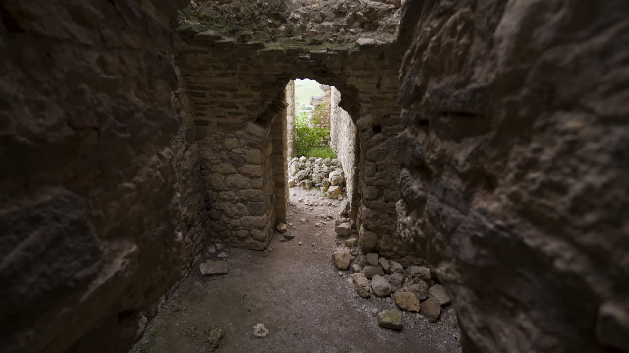 Top-down drift between rough masonry walls toward the main entrance of Bukelon Fortress near Matochina, Bulgaria—archway, rubble and slit openings forming a narrow medieval passage