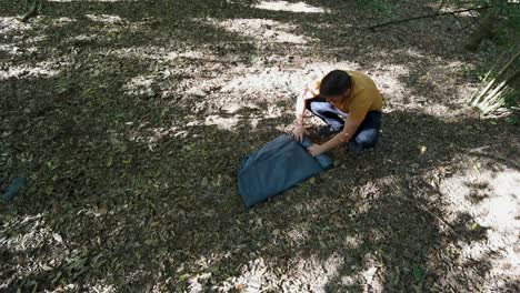 slow motion of man tourist rolling up a tent at forest campsite and packing up to leave