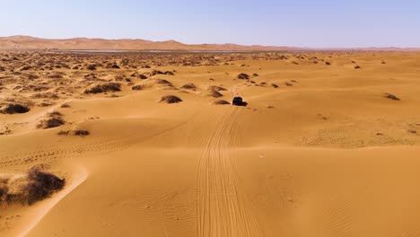 Aerial-view-of-a-pickup-truck-traversing-the-expansive-desert-landscape-of-Tengger-Desert,-Inner-Mongolia-Autonomous-Region,-China