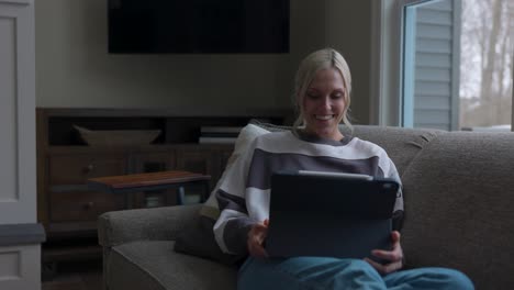 woman walking to the couch to lay down and scroll through tablet while drinking coffee in a nice house