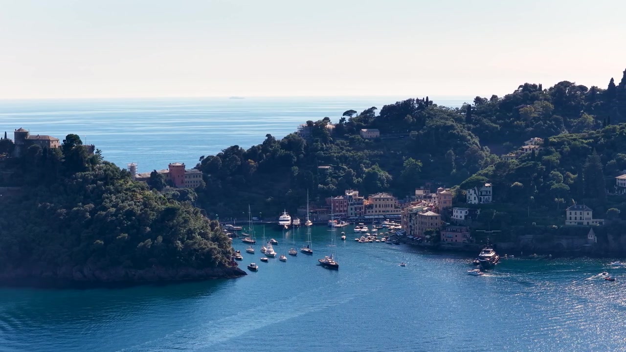 Inquadratura grandangolare di barche ancorate in una suggestiva baia italiana con rigogliose colline verdi.