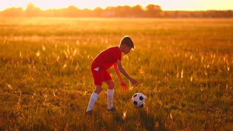 boy junior in a red t-shirt and sneakers at sunset juggling a soccer ball training and preparing to become a football player. the path to the dream. training at sunset and dawn