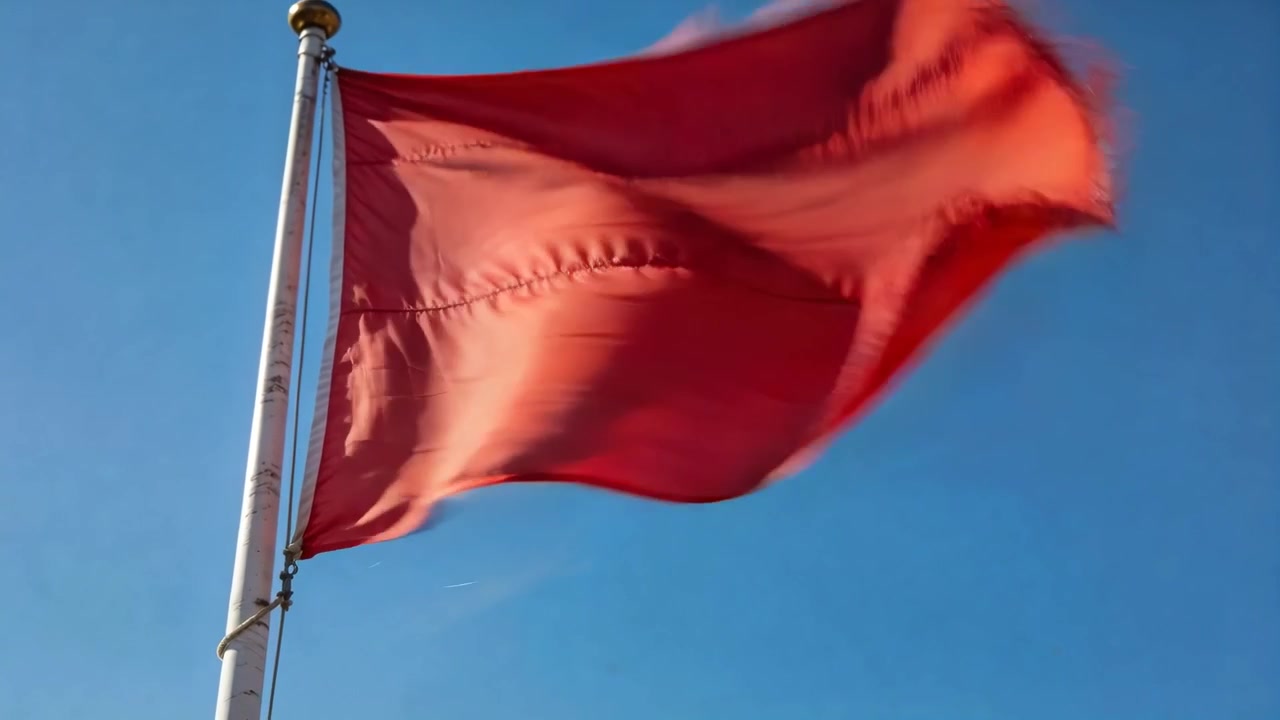 Bendera merah berkibar karena angin kencang, berubah dari menggembung menjadi datar di bawah langit biru cerah, tiang.