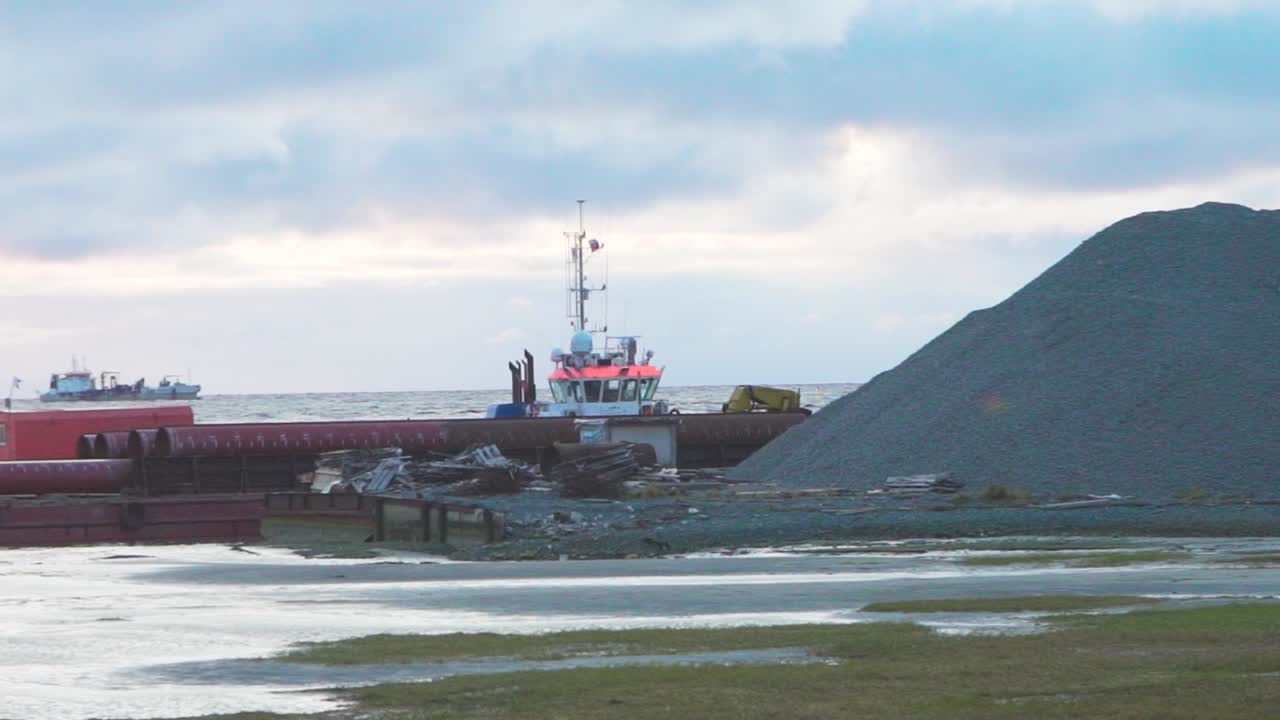 remolcador y barcaza en puerto con tuberías y montones de grava