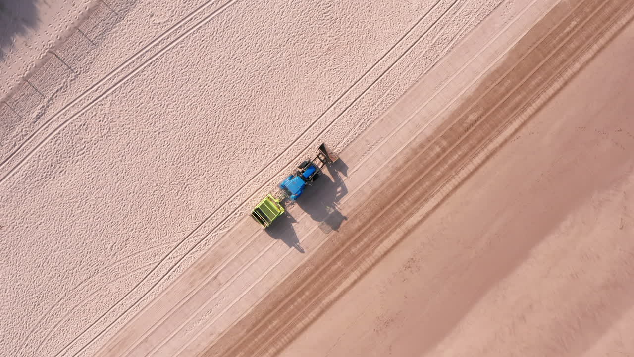 Faldende tracking-optagelse af en traktor med trailer, der renser en sandstrand i North Devon