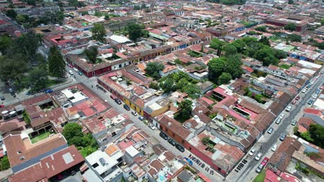 drone aerial footage of car and motorbike street traffic in antigua, guatemala colonial town showing bright colorful red rooftops, and green tree tops