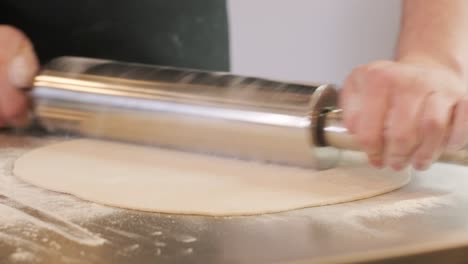 italian pizza chef forming the dough on a floured surface and rolling out a dough