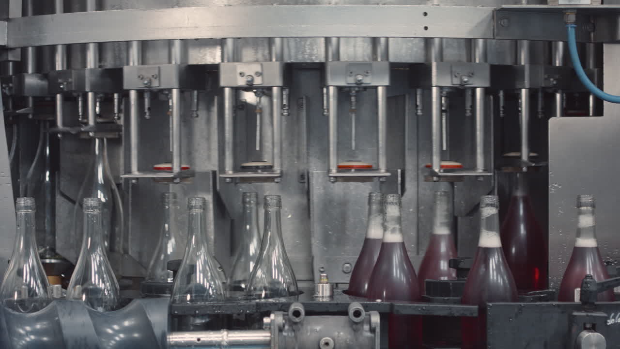 Medium shot showing glass bottles being filled with sparkling wine on an industrial production line.