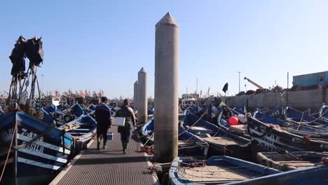 fishermen walking on a dock with numerous blue fishing boats in morocco