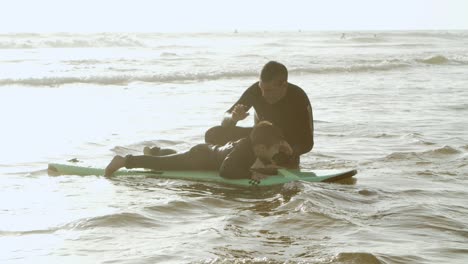 father teaching son standing on surfboard