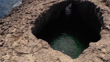 AERIAL:-Flying-backwards-over-famous-Ahrax-tal-Mellieha-Blow-Hole,-Malta