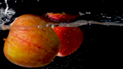 Zwei-Rote-Äpfel-Fallen-Vor-Schwarzem-Hintergrund-In-Zeitlupe-Ins-Wasser