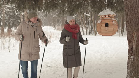 senior couple hiking in snowy park with birdhouse