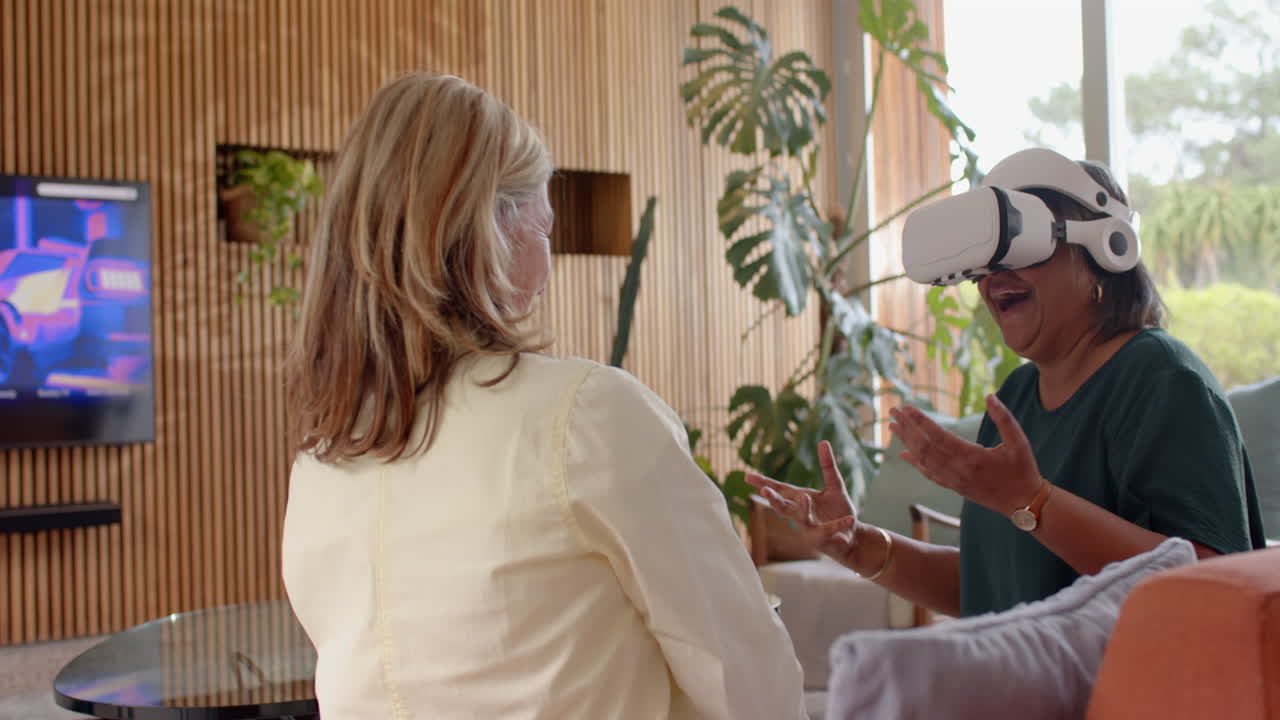 Using VR headset, senior woman excitedly interacting with friend in living room, at home