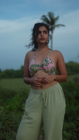 beautiful woman in floral top and green pants posing outdoors at sunset