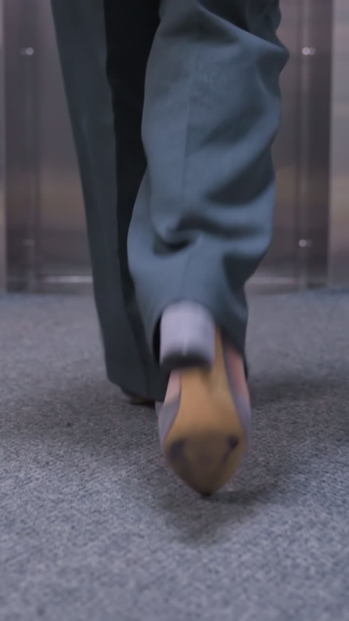 Back view of businesswoman walking confidently in office, wearing stylish gray shoes on office carpet floor, showcasing professional attitude and fashion