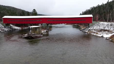 covered bridge with a little bit of snow crossing a river in quebec, canada