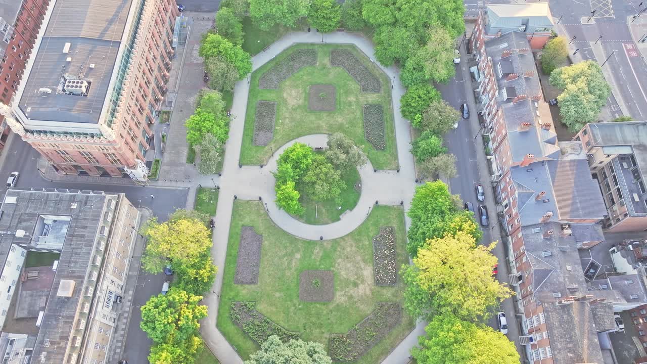 Drone top-down view of Park Square in central Leeds, showing its oval-shaped green space, tree-lined walkways, and elegant heritage buildings surrounding the square