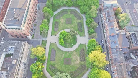 drone top-down view of park square in central leeds, showing its oval-shaped green space, tree-lined walkways, and elegant heritage buildings surrounding the square