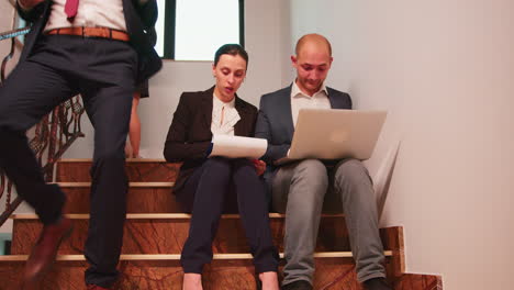 Business-people-analysing-reports-sitting-on-stairs