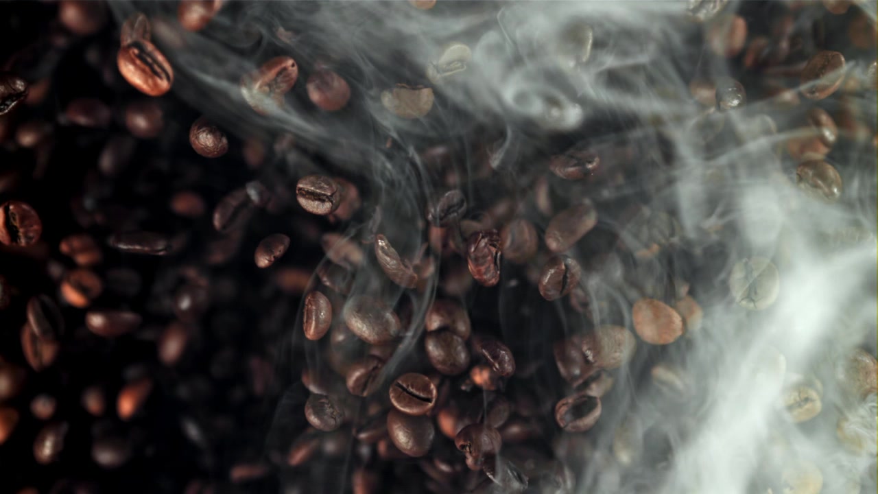 Chicchi di caffè tostati che cadono con fumo aromatico al rallentatore