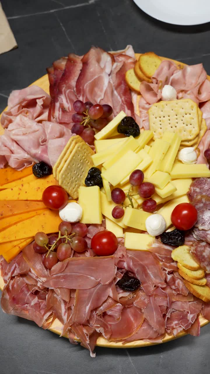 Cena di Natale - Ricco tagliere di salumi e formaggi con prosciutto crudo, prosciutto cotto, formaggi assortiti e cracker. Ripresa dall'alto, scorrevole.