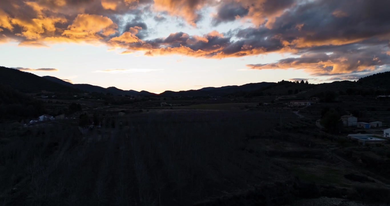 Drone hyperlapse pushing toward dramatic golden sunset skies above farmland and rolling hills near Bullas Spain.
