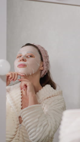 mujer con máscara en la cara hace movimientos repentinos con las manos. mujer morena en bata de baño baila activamente haciendo tratamientos faciales en la ducha en cámara lenta
