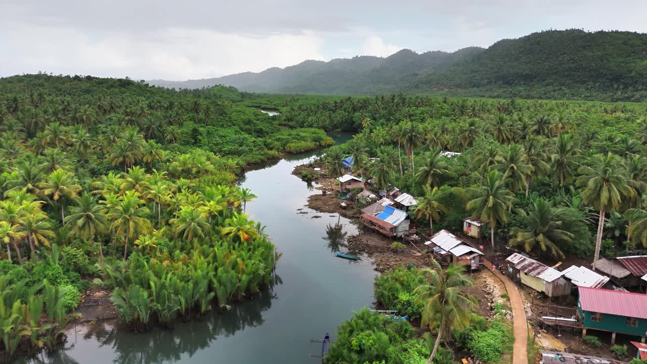 Drone shot over Mataob Maasin Mangrove, Siargao Islands, Philippines, showing lush nipa palms, a winding river, stilt houses, and coconut trees framed by forested hills